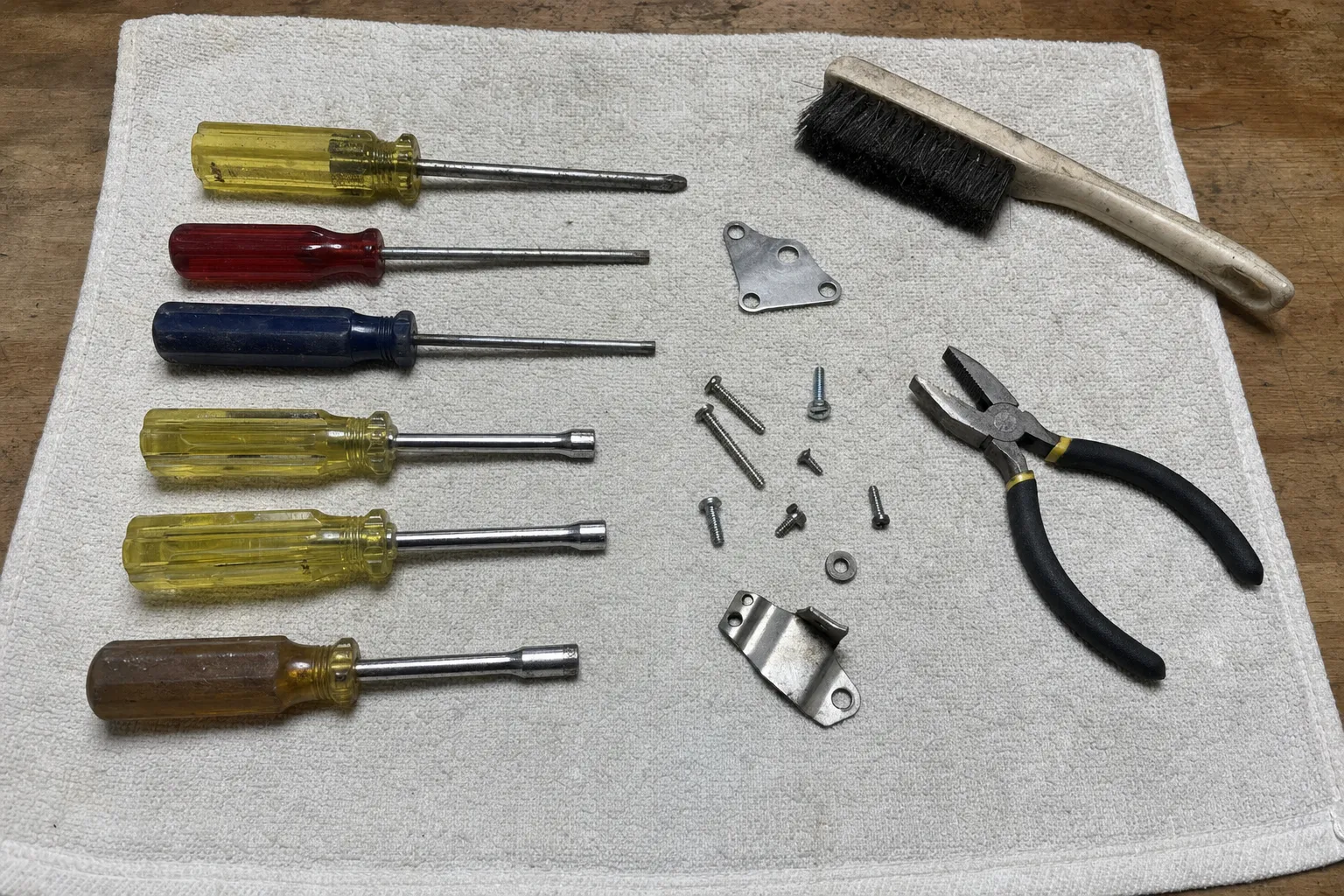 Repair tools laid out on a cloth: screwdrivers, nut drivers, pliers, a wire brush, screws and brackets